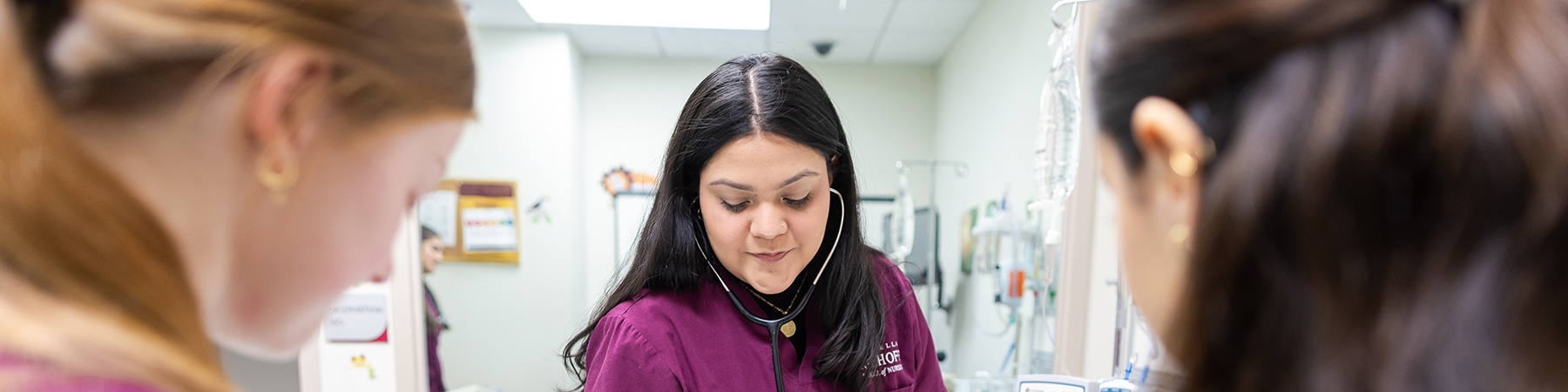 Three nursing students look down as they tend to a manikin in the Lake Shore Campus simulation lab